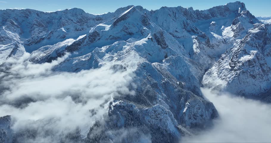 Aerial view of snow-covered mountain peaks piercing through a blanket of clouds, creating a serene winter scene, Garmisch-Partenkirchen, Bavaria, Germany.