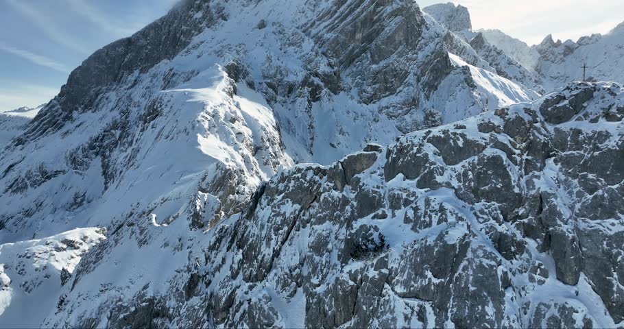 Aerial view of towering snow-capped mountains under a clear sky, their jagged peaks and slopes creating a dramatic contrast of light and shadow, Garmisch-Partenkirchen, Bavaria, Germany.