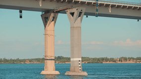 A view from the water looking at massive concrete bridge supports. The calm blue river flows around the piers under a light blue sky. A tranquil scene of modern engineering and transportation - Powered by Shutterstock - Get 15% off with code: PIKWIZARD15
