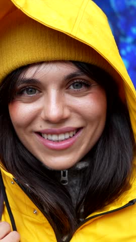 Close up portrait of a beautiful young woman with green eyes wearing a yellow raincoat and beanie, happily smiling while exploring the city of san francisco on a cloudy day
