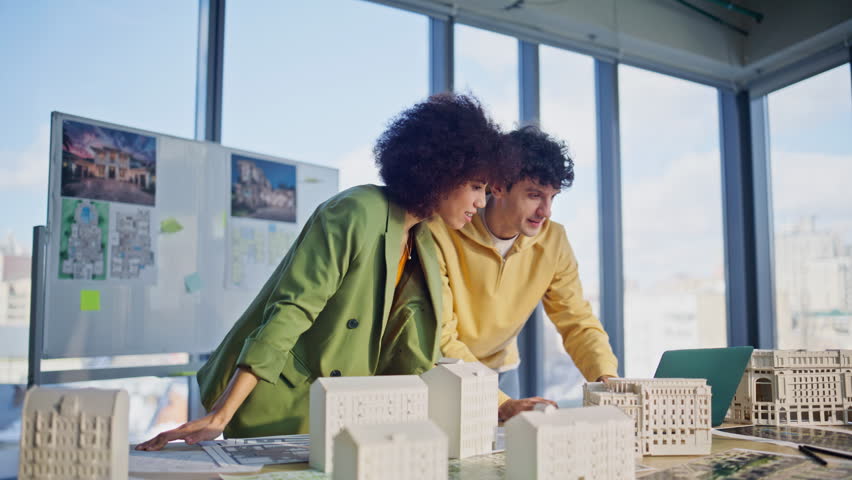 Construction engineers discussing models of residential buildings working together on urban project in office. Multiethnic colleagues working on houses layout. Creative builders planning real estate.