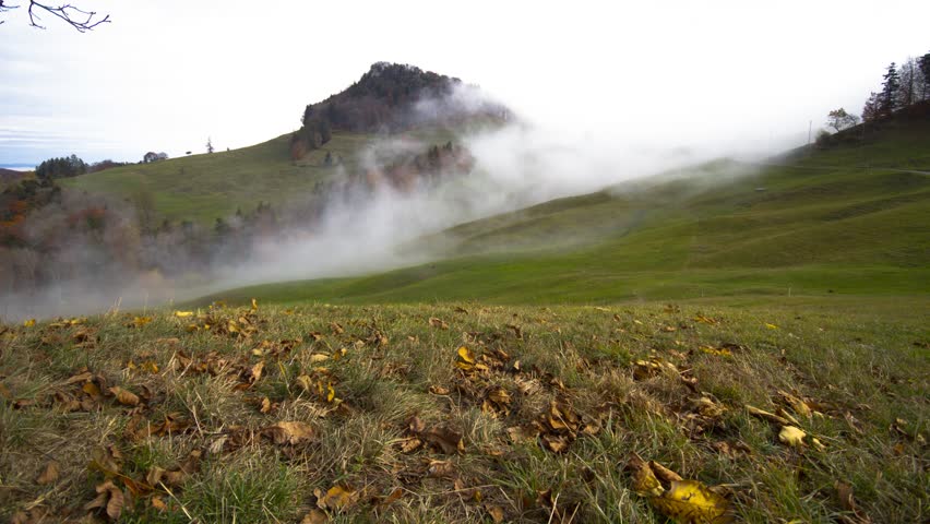 Dramatic View of Thick White Mist Rolling Over Vibrant Green Alpine Hills