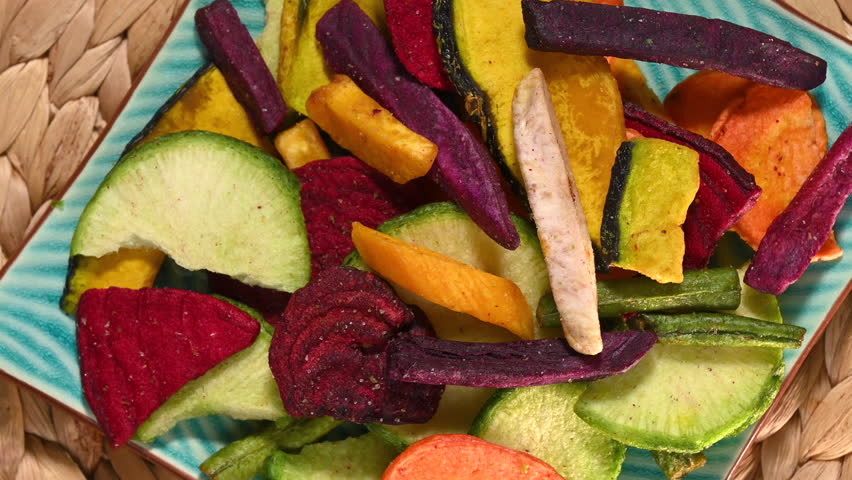 Colorful plate of mixed dried vegetable chips slowly rotating on a wicker placemat