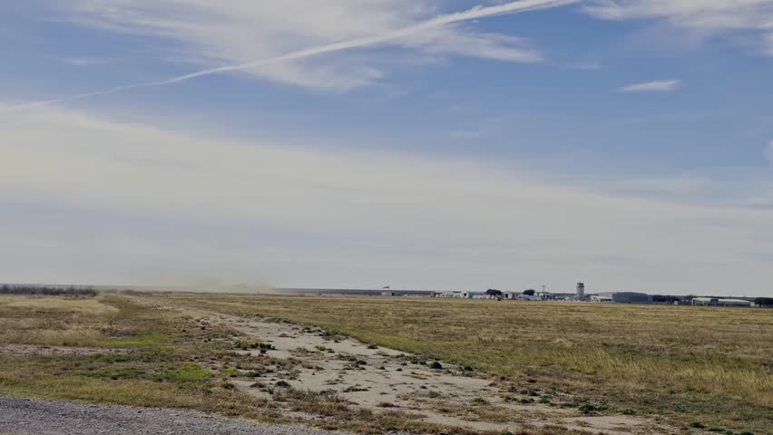 A powerful C-17 Globemaster III taking off from a distant airport runway. The aircraft ascends against a backdrop of a clear blue sky, kicking up dust as it begins its journey.
