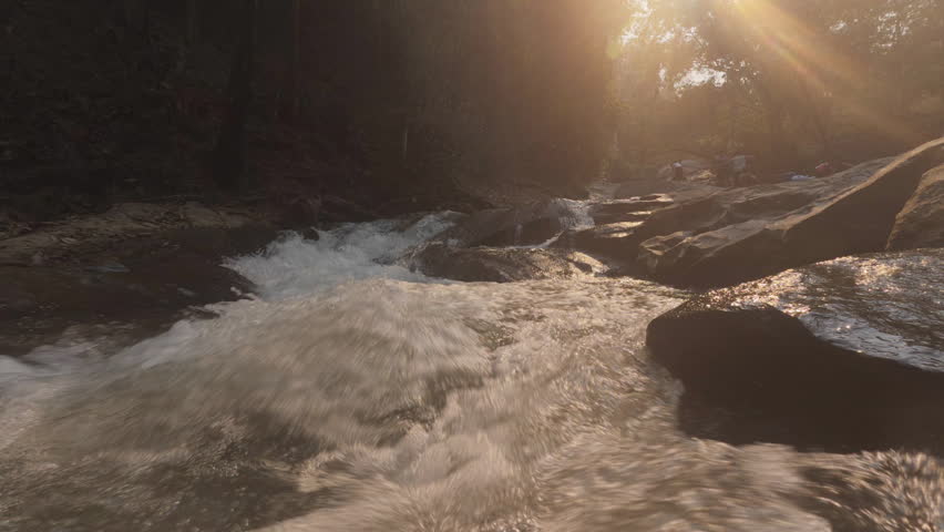 A tranquil scene of river rapids cascading over rocks, bathed in warm sunset light filtering through the surrounding trees