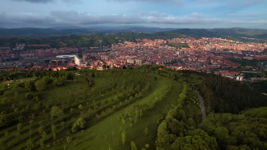 Drone flying forward over green hills revealing Bilbao city skyline, buildings and urban landscape. Scenic aerial view of Basque Country in northern Spain. High quality 4k footage