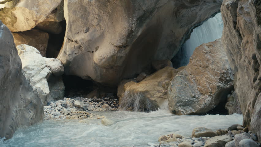 Clear river flowing through a rocky canyon with large boulders and small waterfalls. Scenic natural landscape with detailed stone textures and layered rock formations.