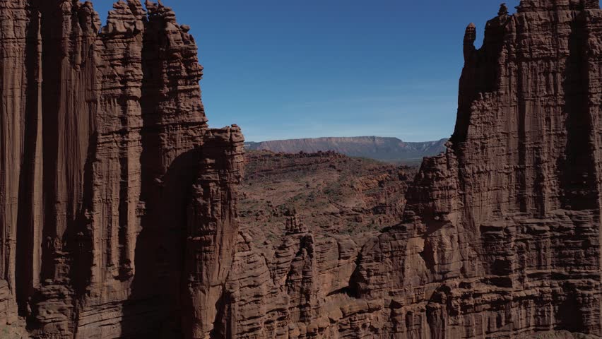 Aerial pullback shot of dramatic Fisher Towers spires, dark red Cutler sandstone capped by Moenkopi layers.