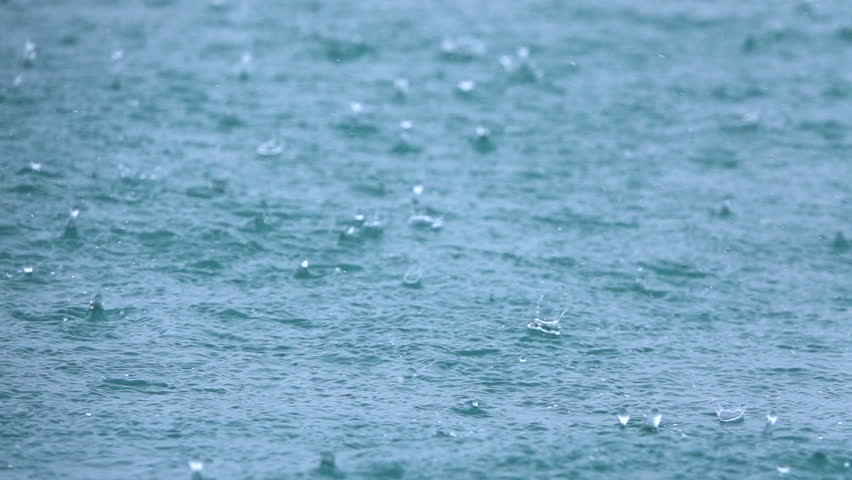CLOSE UP, DOF, SLOW MOTION: Raindrops falling and splashing into blue surface of wavy ocean on a tropical island. Tiny splashes and ripples during heavy shower in rainy season in exotic Indonesia.