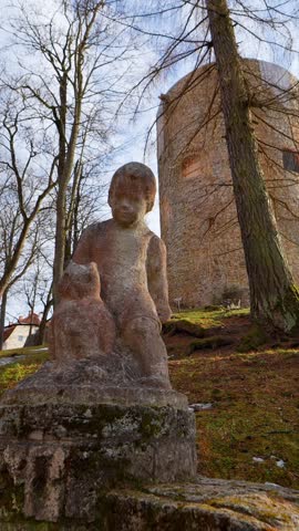 Weathered stone statue of a child beside an old castle tower, capturing historic park atmosphere, aged sculpture detail, and quiet heritage scenery in soft daylight.