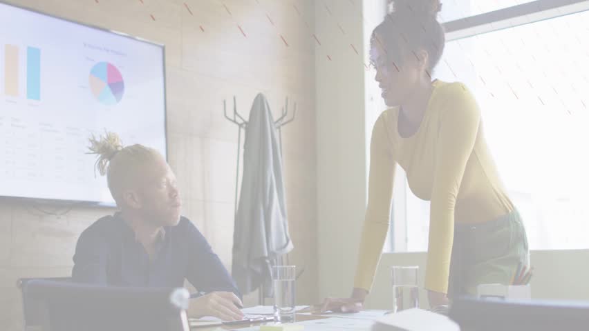 Woman leaning and gesturing, initiating business discussion with charts while man using laptop docs. Collaboration, meeting, conference, graphs, presentation, teamwork, daylight