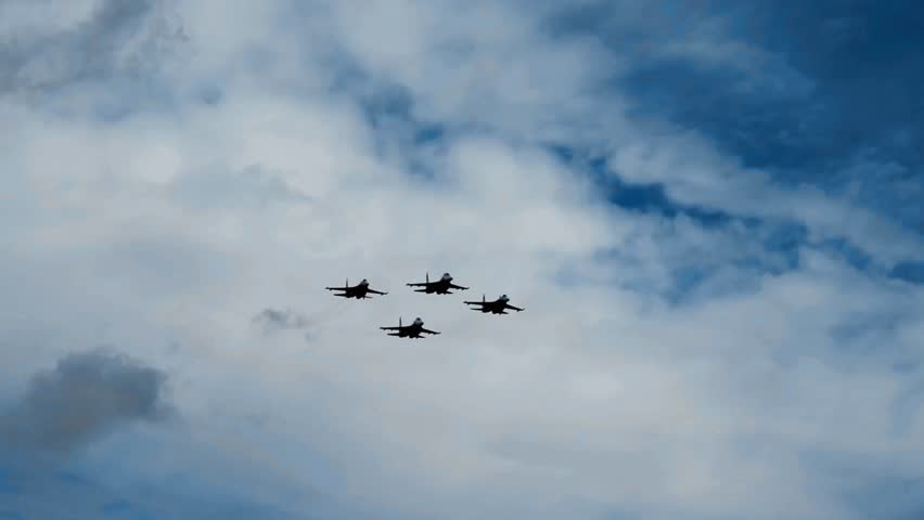 Cinematic 4K footage of four military fighter jets flying in formation against a blue cloudy sky. An impressive aerial display of air force power, speed, technology, and precision maneuvers.