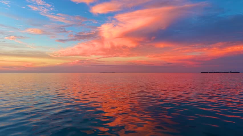Slow motion view of a calm ocean into the during summer sunset with orange and red clouds and reflections in the water