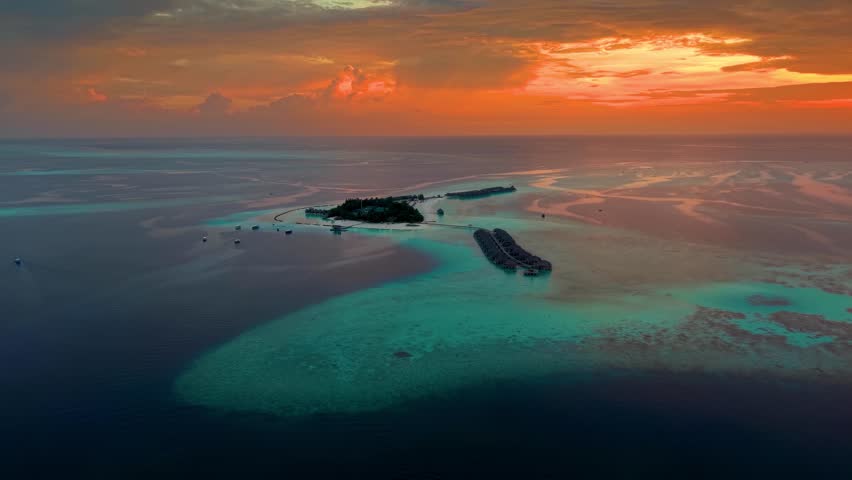 A beautiful paradise island in the Maldives with water bungalows over the turquoise ocean with shining coral reefs during a dramatic sunset
