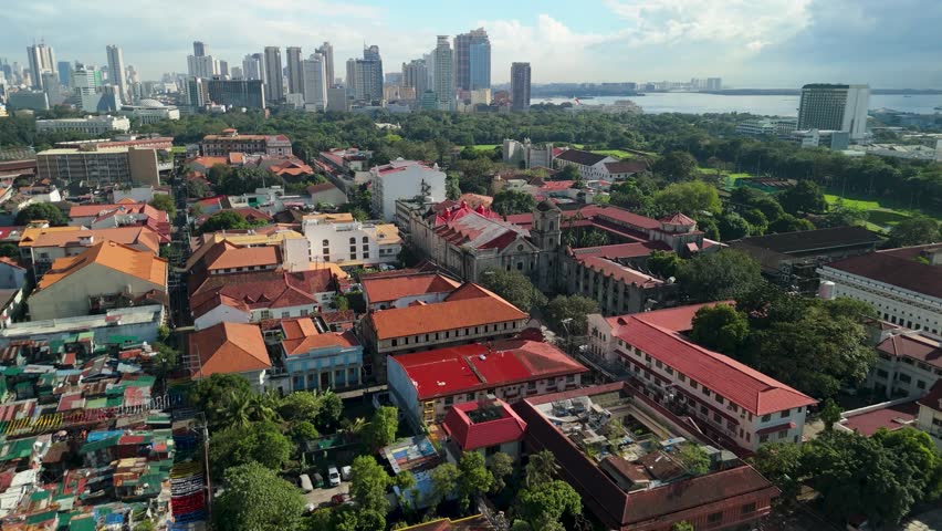 Cinematic aerial approach toward San Agustin Church in Intramuros Manila revealing UNESCO World Heritage stone baroque complex with convent, bell tower, and Manila Bay backdrop