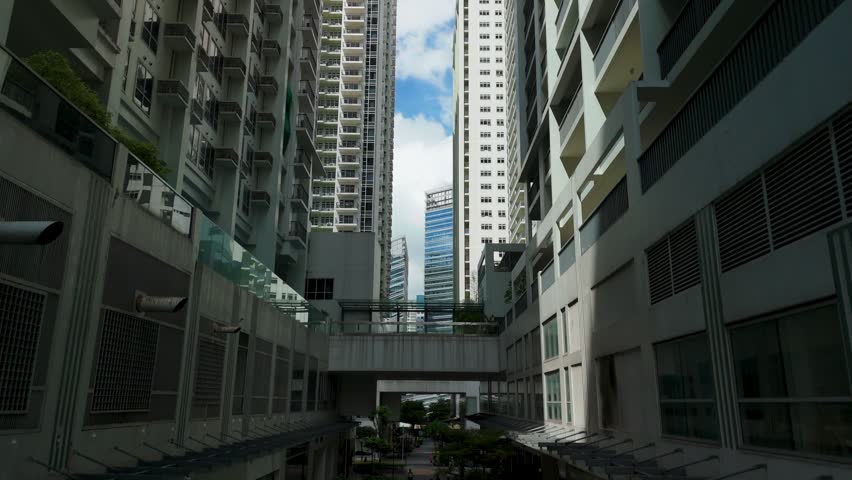 Drone rises through narrow urban canyon between modern high-rise condominium towers in Bonifacio Global City revealing blue sky above balconies