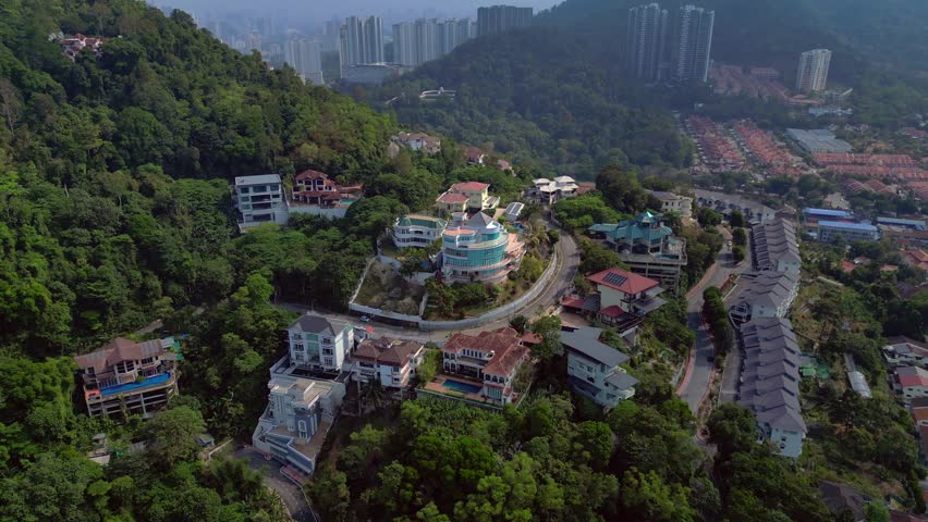 Penang, Malaysia, hillside residential area featuring luxury homes, modern villas, and affluent housing, surrounded by lush green trees. Unique aerial view descending panorama drone