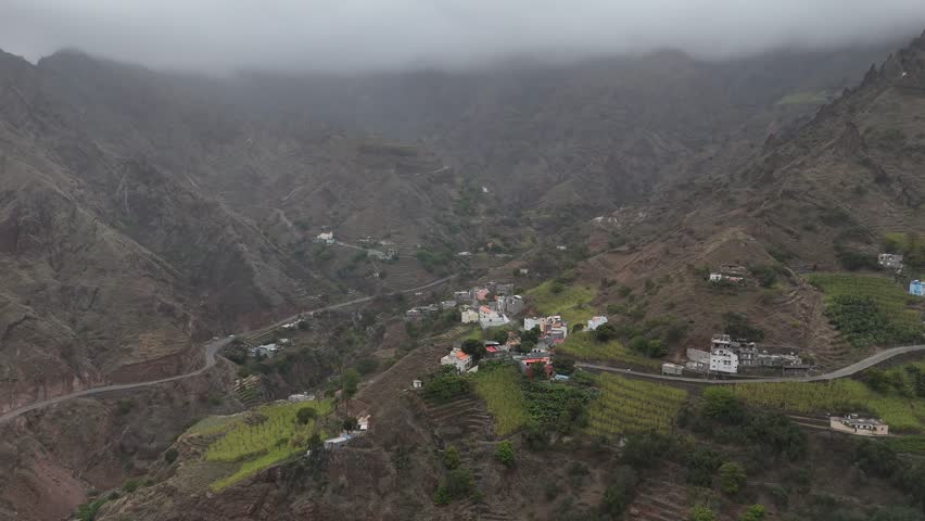 drone orbit around mountain village in Santo Antao, Cape Verde. Scenic terraced fields and colorful houses jagged volcanic peaks under a misty, dramatic sky