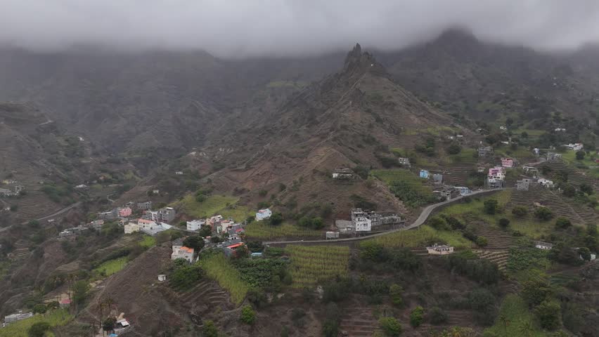 Aerial view of Fontainhas mountain village in Santo Antao, Cape Verde. Scenic drone shot of colorful houses nestled in lush green valley with misty volcanic peaks and winding coastal roads