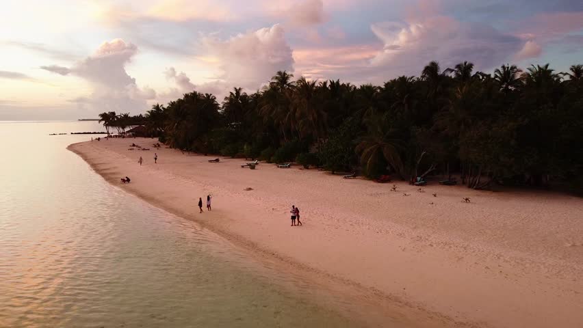 Drone perspective of sandy shoreline, calm sea and dramatic clouds at dusk.