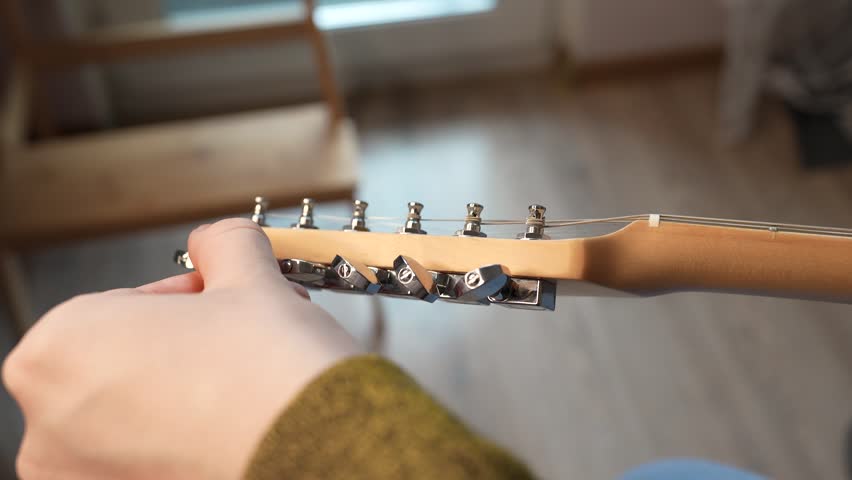 A man Tuning his guitar and playing it. Top lock tuners on double cut electrical guitar.
