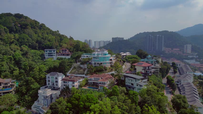 Residential properties and houses built on a tropical hillside in Penang, Malaysia, showcasing contemporary architecture and urban development. Majestic aerial view fly push forward panorama drone