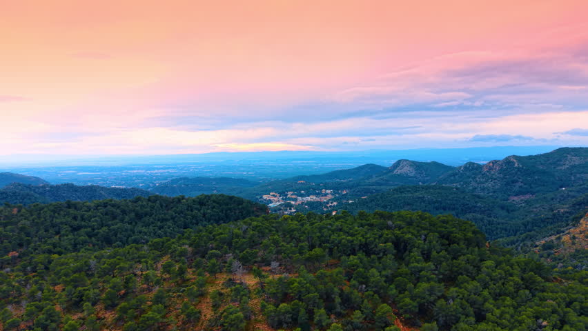 Sunset over mountainous forest landscape with pink and orange sky. Panoramic view of forested hills and a distant valley under a vibrant sunset sky with pink clouds.