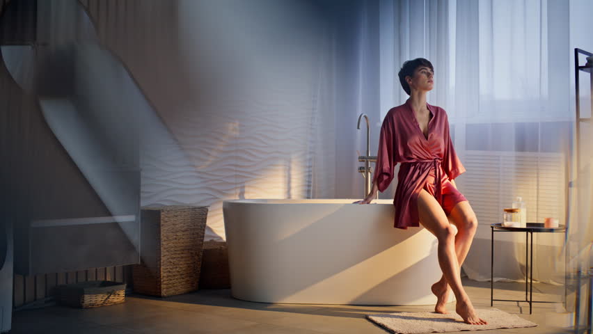 Young woman sitting bathtub waiting spa at morning home. Satisfied relaxed brunette enjoying beauty routine. Silk gown luxury lady relaxing alone. Pretty model preparing to foamy bath procedures 