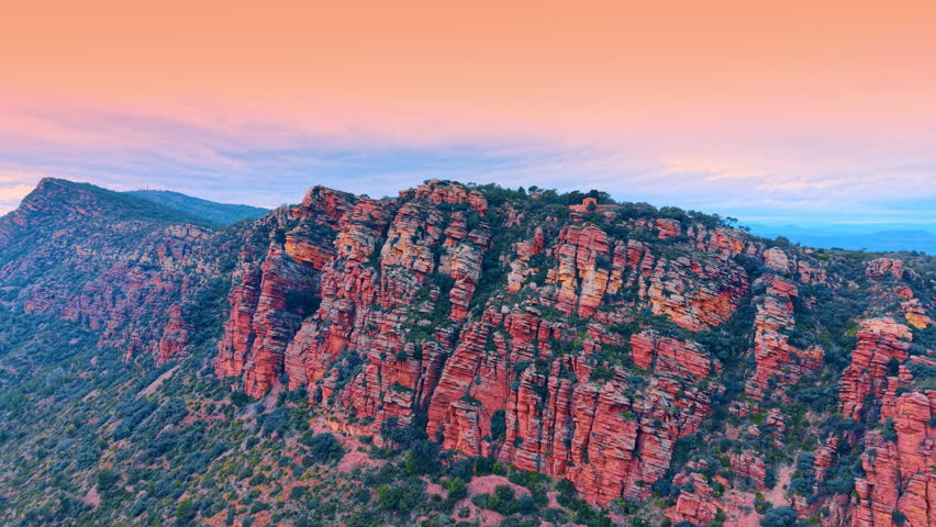 Panoramic sunset over red sandstone cliffs and forested mountains. Wide landscape shot of red rocky mountains under a colorful evening sky with green forest.