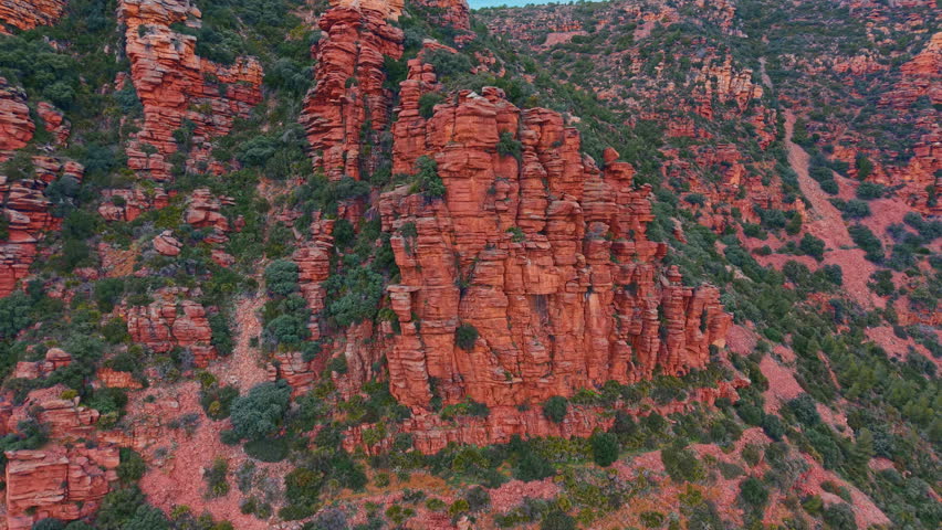 Red sandstone columns and Mediterranean scrub. A rock pillars surrounded by green bushes and forest on a slope.