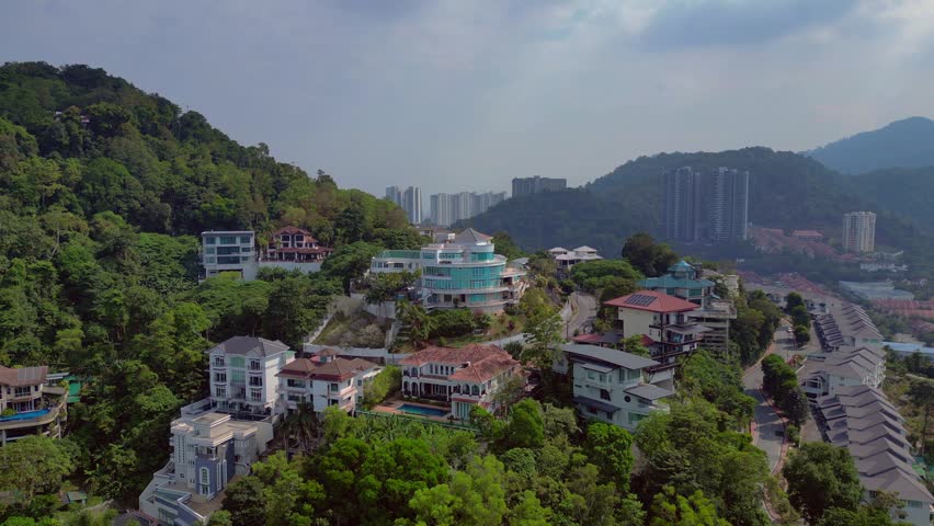 Penang, Malaysia, hillside residential area featuring luxury homes, modern villas, and affluent housing, surrounded by lush green trees. Smooth aerial view