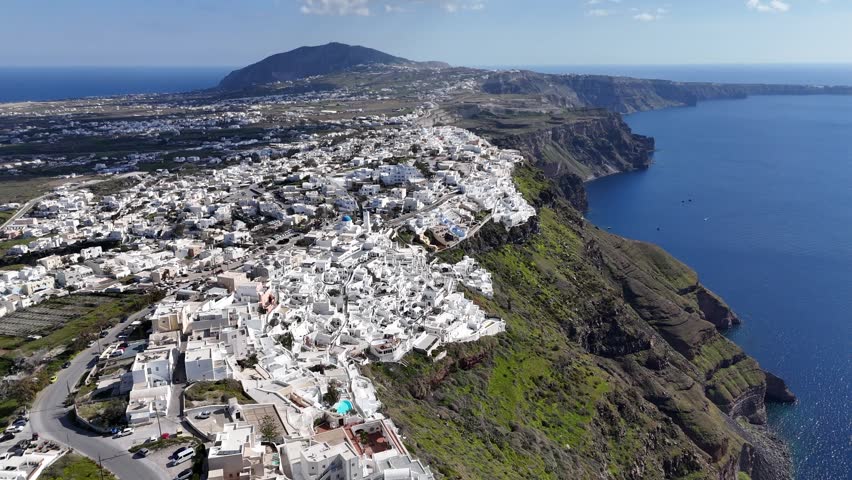 Breathtaking wide aerial panorama of Oia village in Santorini, Greece. The white architecture contrasts beautifully with the dark volcanic cliffs and the deep blue Aegean Sea