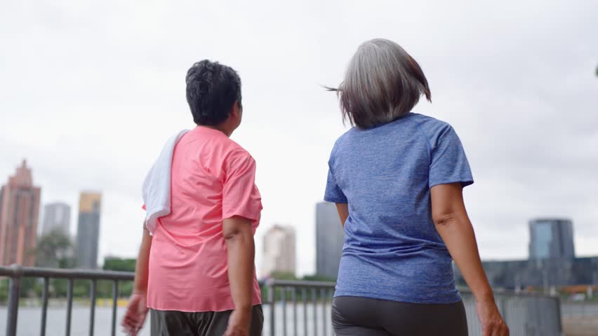 Two happy Asian senior women walking exercise outdoors in modern city. Active elderly older friends wearing sportswear, enjoy healthy lifestyle, workout and fitness activity in urban park environment.