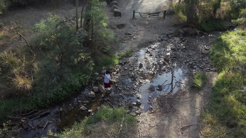 A girl stands by a rocky stream at Warrandyte Park during twilight. The serene setting is highlighted by gentle evening light, creating a tranquil and peaceful atmosphere.