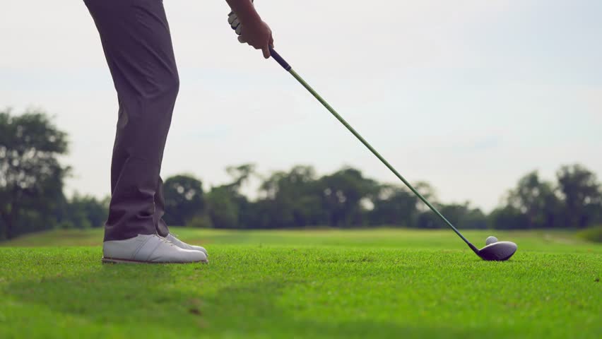 Close up of professional golfer swinging club on a scenic golf course. The shot captures the precise moment of striking the golf ball on the well maintained green fairway.