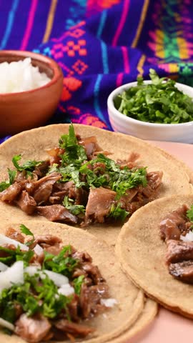 Mexican food. Placing chopped onion with a spoon on top of some carnitas tacos with cilantro