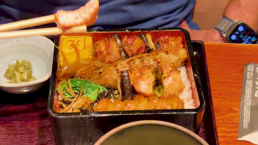 Close up of grilled chicken skewers over rice in lacquer box.