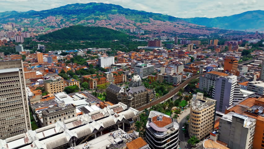 Aerial drone view of downtown Medellín, Colombia, featuring Botero Plaza and the metro, with dense urban architecture, public space, and dynamic city life seen from above.