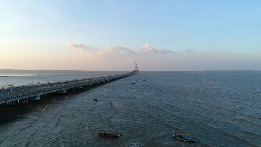 A stunning high-angle drone shot capturing the expansive Suramadu Bridge as it stretches across the Madura Strait, connecting Surabaya on Java island to Madura island under a clear sky