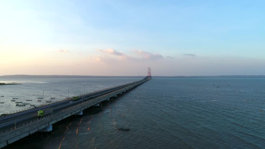 Aerial perspective of the Suramadu Bridge, the longest bridge in Indonesia, showing vehicles traveling along the expansive highway connecting Surabaya and Madura Island across the calm blue waters of the Madura Strait during a clear day