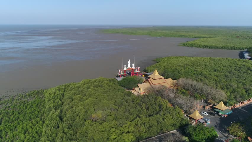 Aerial view of the iconic Sanggar Agung Temple (Hong San Tang) in Surabaya, Indonesia, featuring the magnificent Goddess Kwan Im statue and twin dragons overlooking the serene mangrove coast