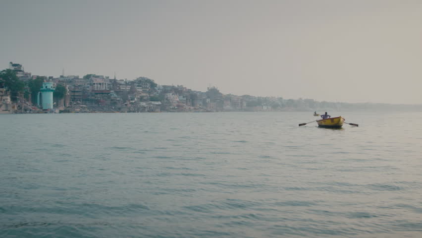 Lone fisherman paddling a small yellow boat on the misty Ganges river with Varanasi city in background