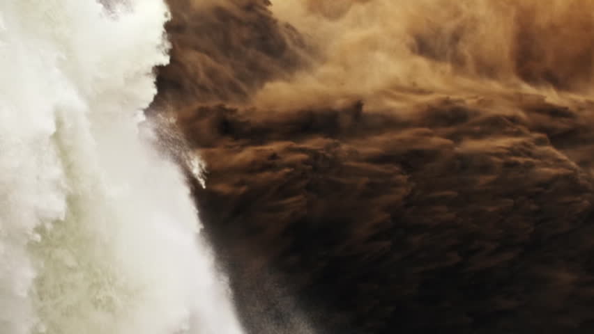 Detail of a powerful waterfall crashing into a raging brown river creating mist and spray