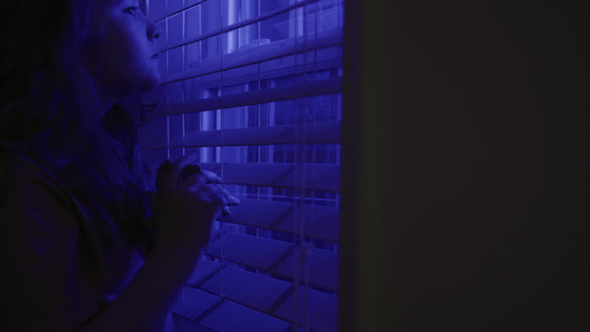 Siren flashes while child hiding in night window in fear. Siren light with kid hides indoors. Siren lights scared child portrait. Siren danger around lone kid.