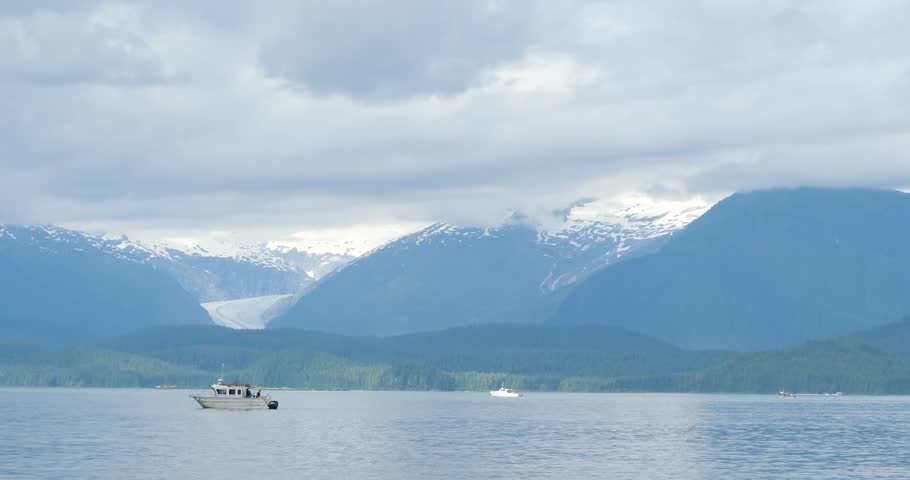 Recreational vessels and Mendenhall Glacier and the surrounding mountains covered by clouds in the background, Alaska.
