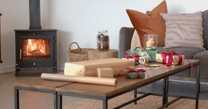 Fire crackling in wood stove flickering candlelight across coffee table with gift wrapping supplies. Cozy, festive, rustic, ambient, warm, homely, seasonal - Powered by Shutterstock - Get 15% off with code: PIKWIZARD15