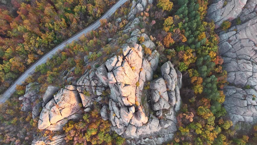 Overhead aerial view of a curving road through colorful autumn woodland and rocky terrain.