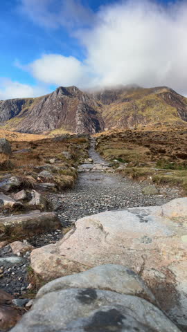 Hiker at Cwm Idwal Nature Reserve in the Ogwen Valley, part of the Eryri Snowdonia National Park. The hiking trail leads toward the dramatic rock cleft of Twll Du Devil
