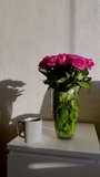Human hand pours clear water from glass kettle into white ceramic mug, placed beside fresh pink rose bloom in transparent vase, bathed by warm morning sunlight, casting gentle shadow on textured wall. - Powered by Shutterstock - Get 15% off with code: PIKWIZARD15