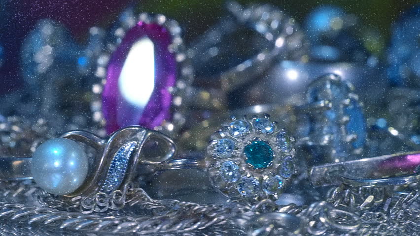 Beautiful shiny, sparkling golden jewelry on a glass surface with bright flares is rotation. View through sparkling particles. Macro. Closeup. Shallow depth of field